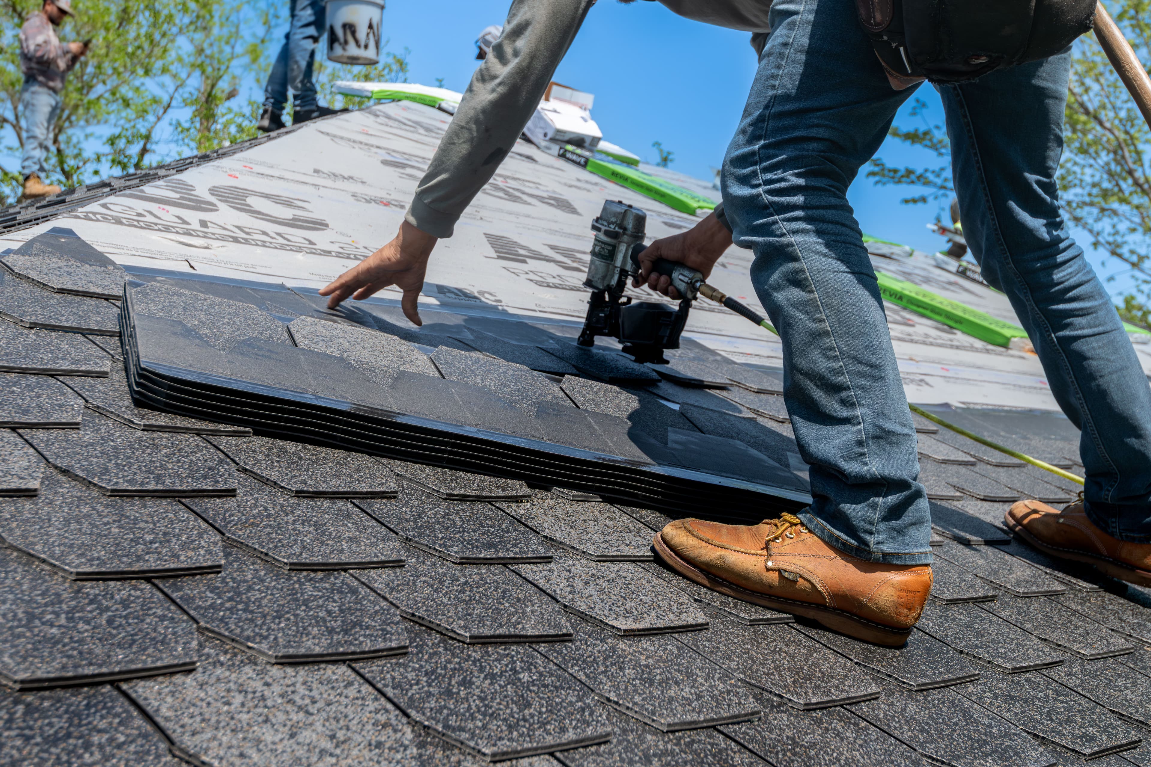 Roofer nailing down architectural shingles on a sunny day